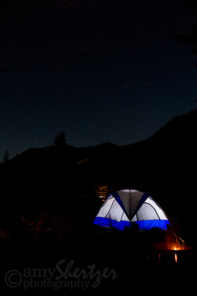 A tent and campfire glow under a starry Montana sky