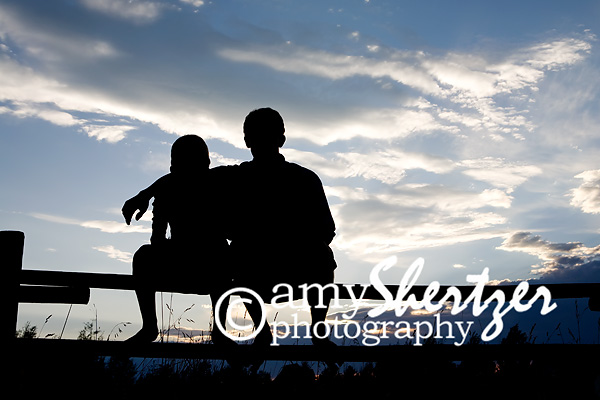 Brothers sit on a split rail fence, silhouetted against a beautiful Montana sky