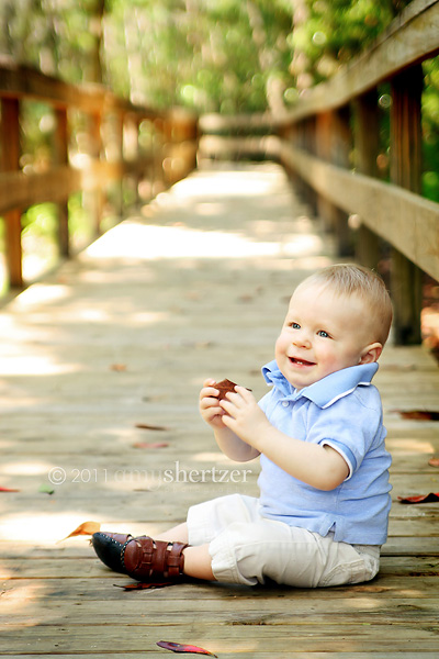 A baby smiles on a boardwalk at the park.