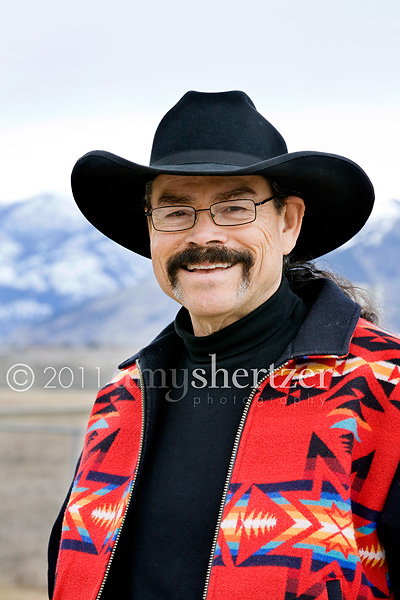 A rancher poses in front of mountains for a professional head shot.