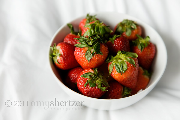 A bowl of red strawberries pops on a white sheet.