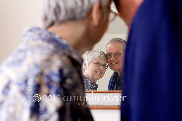 An elderly couple looks into a mirror together.