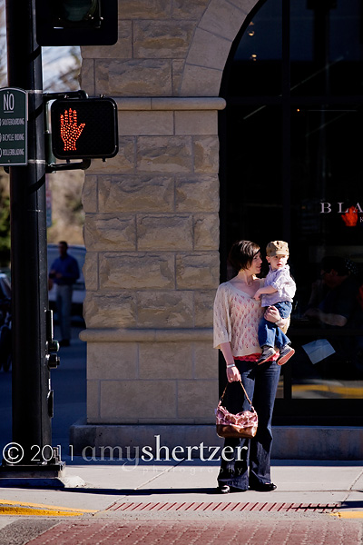 A mother and her son wait on the corner in order to cross the street.