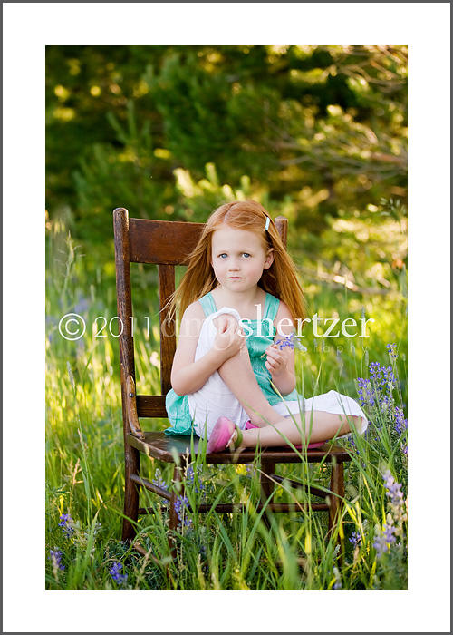 A beautiful red-headed girl in a field of green sitting on a chair.